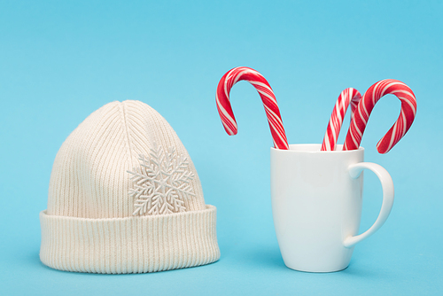 white beanie and candy canes in mug on blue background