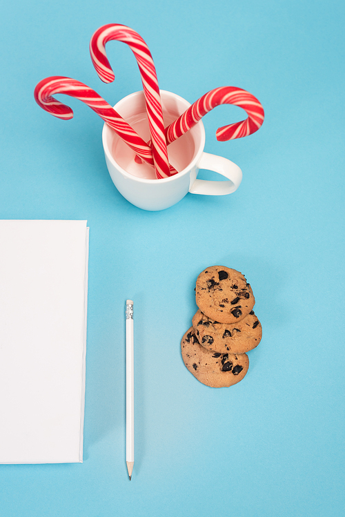 top view of chocolate cookies, candy canes and blank notebook on blue background