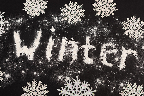 top view of word winter and snowflakes on black background