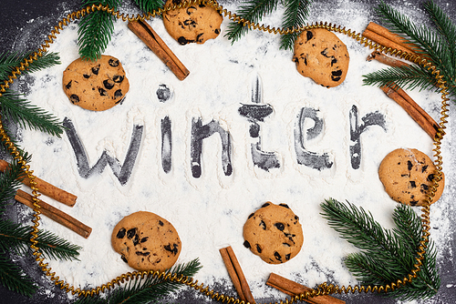 top view of word winter, fir branches and chocolate cookies on black background