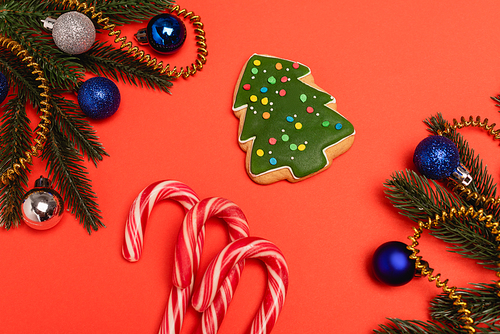 top view of decorated Christmas tree, cookie and candy canes on red background