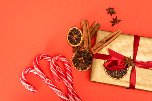 top view of gift with spices and candy canes on red background