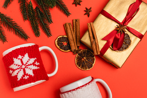 top view of Christmas tree, gift with spices and mugs on red background