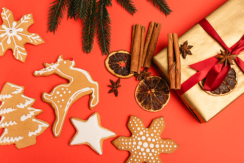 top view of Christmas tree, gift with spices and gingerbread cookies on red background