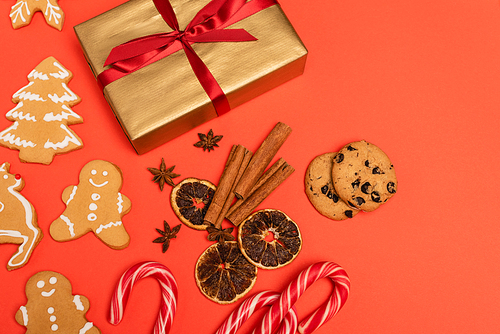 top view of gift, candy canes, spices and gingerbread cookies on red background