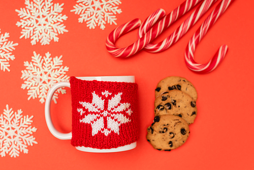 top view of chocolate  cookies, candy canes, snowflakes and mug on red background