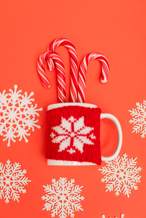 top view of candy canes, snowflakes and mug on red background