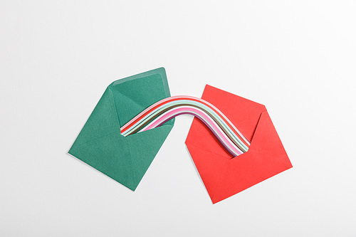 top view of green and red envelopes with multicolored rainbow on grey background