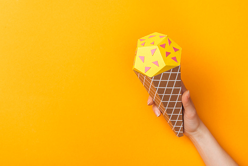 cropped view of young woman holding paper ice cream cone isolated on orange with copy space
