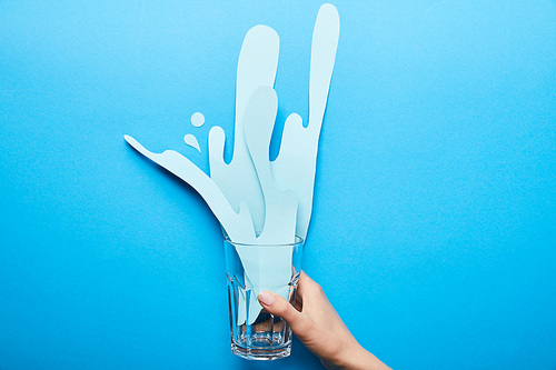 cropped view of woman holding glass with paper cut splash on blue background