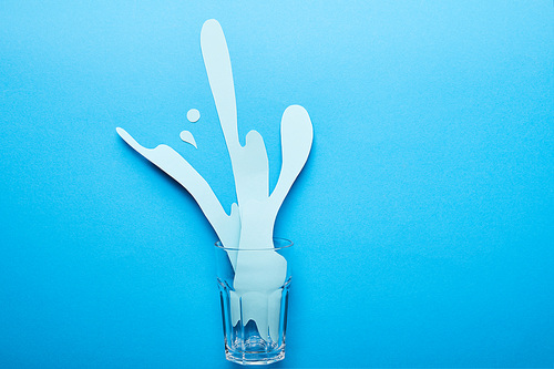 top view of glass with paper cut water splash on blue background