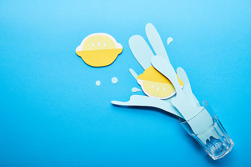 top view of glass with paper cut water splash and lemons on blue background with copy space