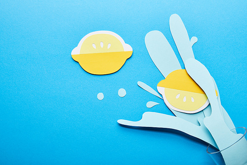 top view of paper cut water splash with lemons near glass on blue background
