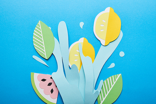 top view of paper cut water splash with lemons, leaves and watermelon on bright blue background