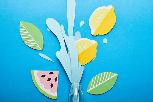 top view of bottle with paper cut water splash, lemons, leaves and watermelon on blue background