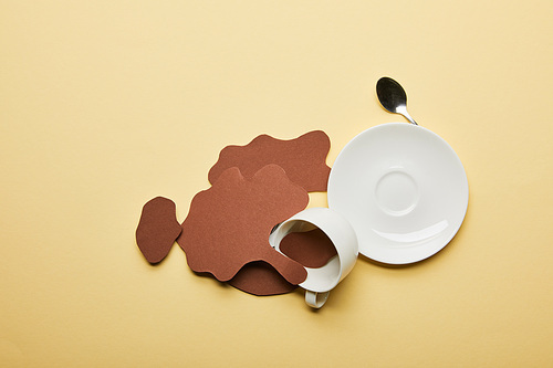 top view of paper cut coffee spills near cup, saucer and spoon on beige background with copy space