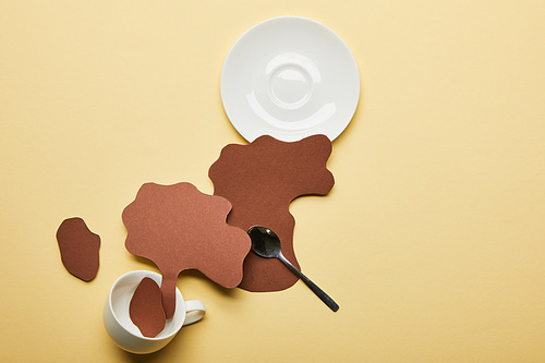 top view of paper cut coffee spills near cup, saucer and spoon on beige background