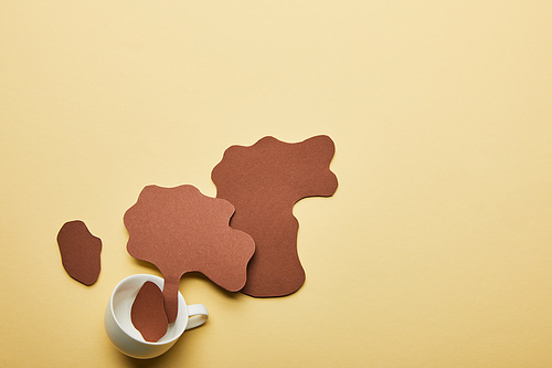 top view of paper cut coffee spills near cup on beige background