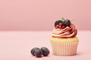 sweet cupcake with cream and grapes on pink surface