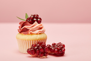 sweet cupcake with cream and garnet on pink surface