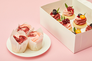 box and plate with sweet cupcakes on pink surface
