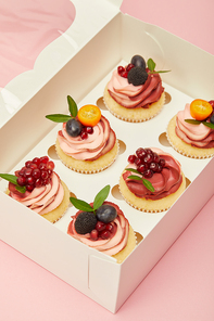 sweet cupcakes with fruits and berries in box isolated on pink