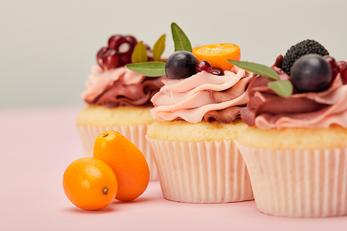 selective focus of cupcakes with kumquats on pink surface