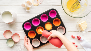 cropped view of woman pouring liquid dough in cupcake pan on table