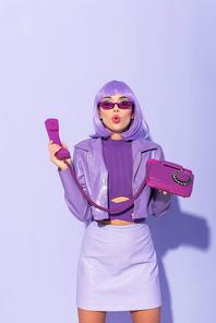 shocked young woman dressed in doll style with retro telephone on violet colorful background