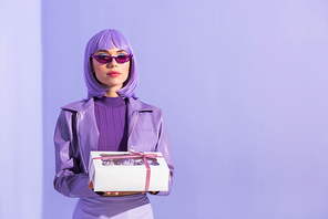 young woman dressed in doll style with cupcake box on violet colorful background