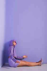 young woman dressed in doll style sitting on floor on violet colorful background