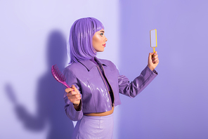 young woman dressed in doll style with hair brush and mirror on violet colorful background