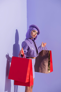 young woman dressed in doll style with red shopping bags on violet colorful background