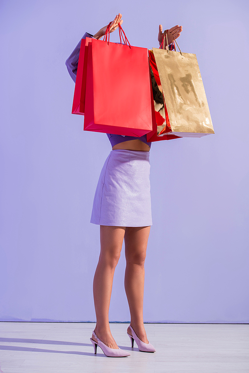 young woman dressed in doll style with red shopping bags on violet colorful background