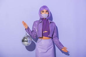young woman dressed in doll style in medical mask with disco ball on violet colorful background