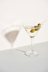 Olives in glass of martini and shadow on white background