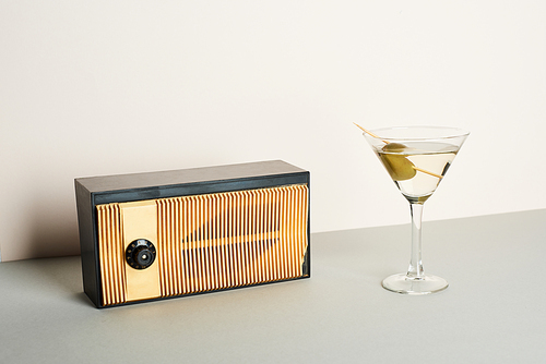 Vintage radio with glass of martini cocktail on grey surface