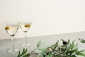 Two glasses with cocktails and olive branch on grey surface isolated on white