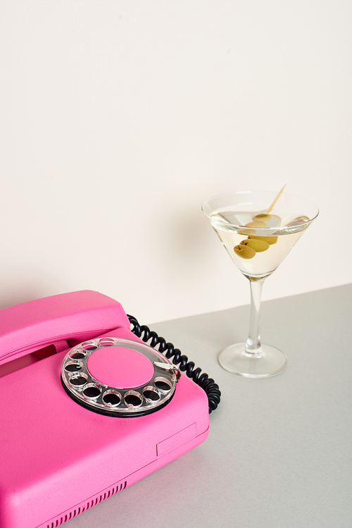 Vintage pink telephone with glass of cocktail on white background