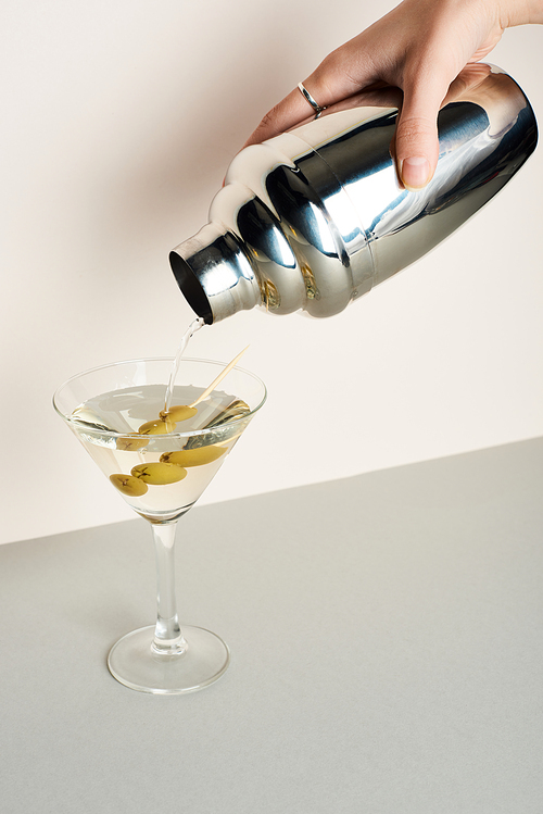 Cropped view of woman pouring martini from shaker in glass with olives