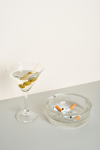 Ashtray with cigarette butts and cocktail on grey surface, isolated on white