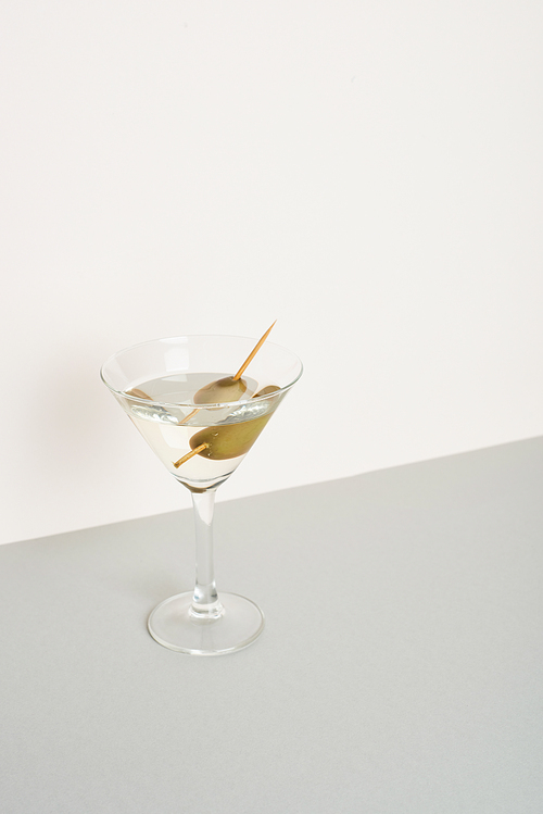 Glass of vermouth with olives on grey surface isolated on white