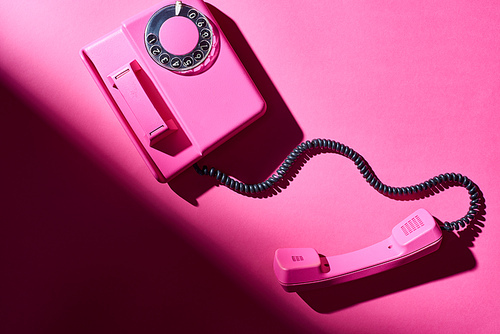 Top view of pink telephone with shadow on bright surface