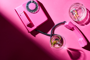 Top view of cocktail and retro telephone beside astray with cigarette butts on pink surface