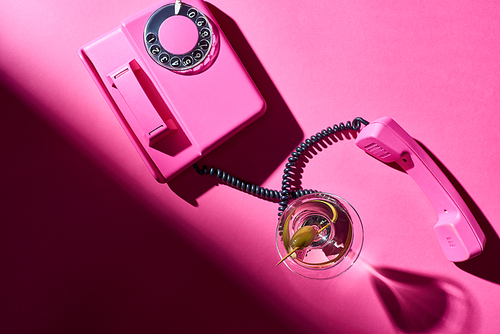 Top view of martini in glass with retro telephone on pink background
