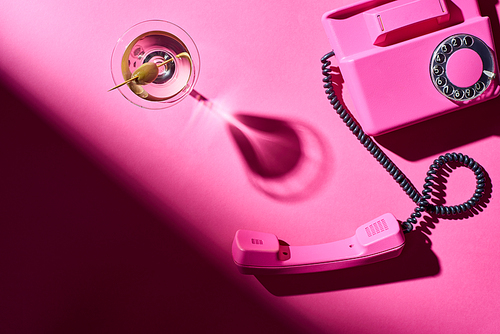 Top view of glass with martini and retro telephone on pink background