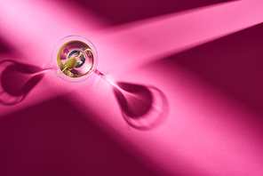 Top view of martini cocktail with shadows on pink surface
