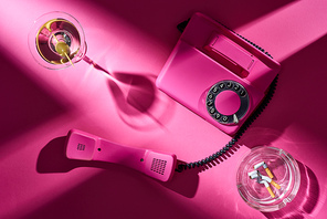 Top view of pink telephone, cocktail and astray with cigarette butts on pink surface