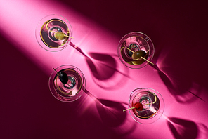 Top view of cocktails with olives on pink background with shadows