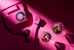 Top view of vintage telephone and cocktails with shadow on pink background
